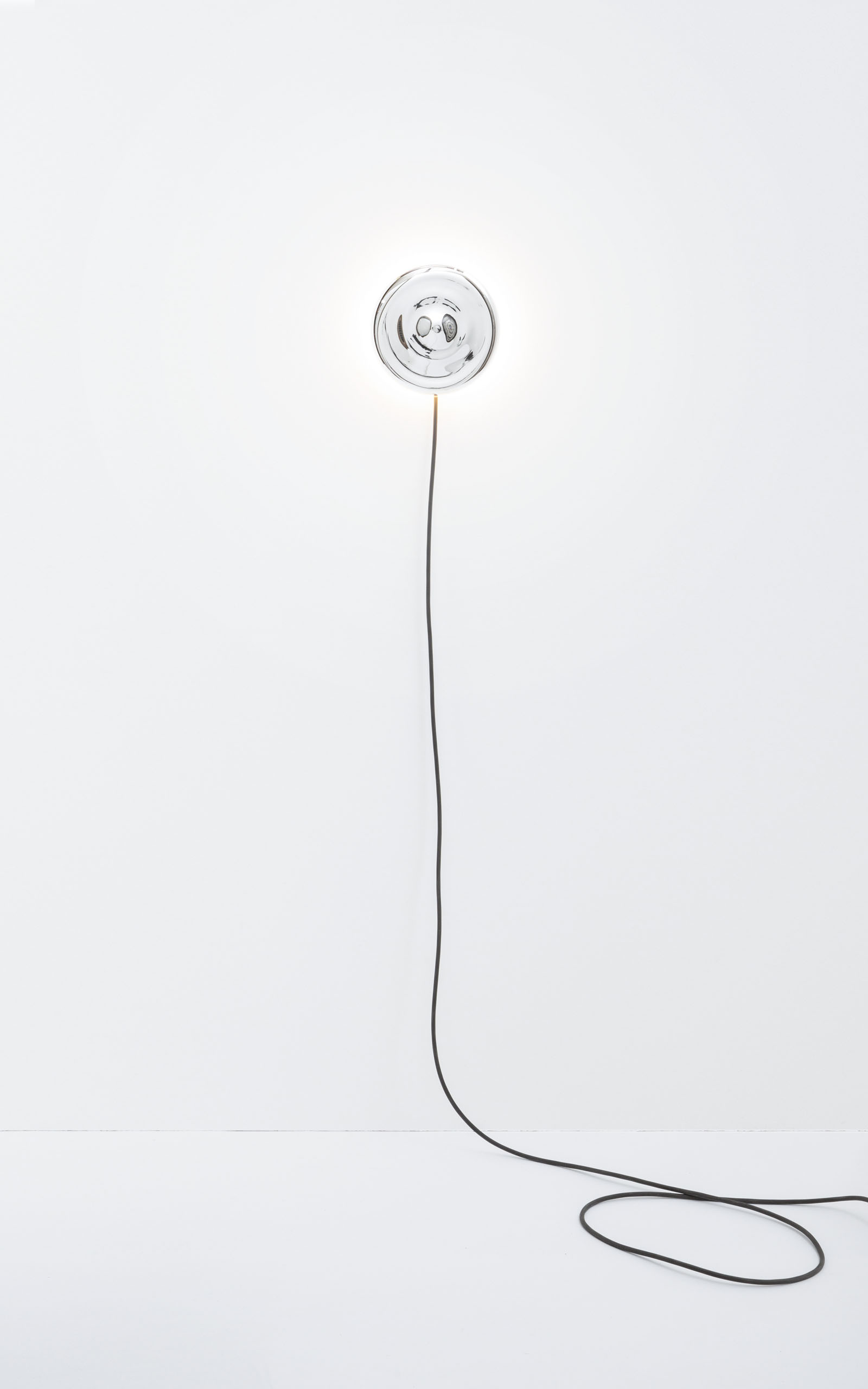 The mirrored body of the wall light is hanging from the wall with the cable starting to curl on the floor.