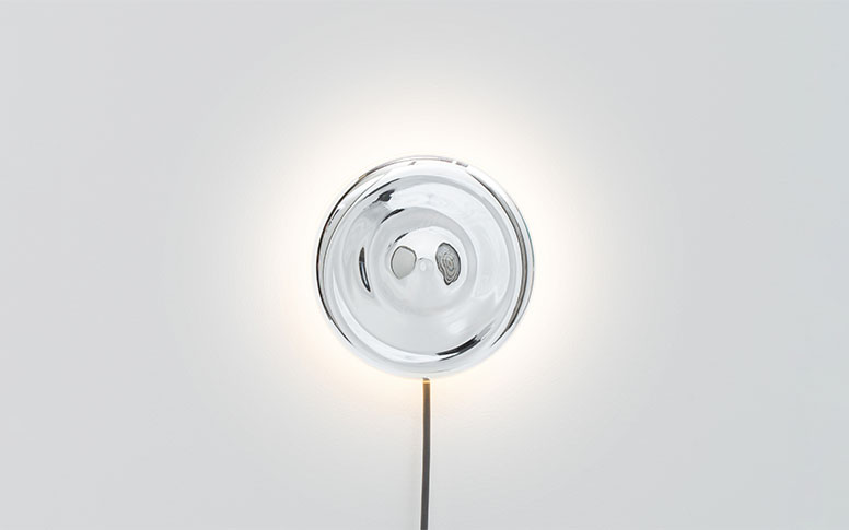 A wall mounted light that consists of a mirror disc and the cable hanging down.